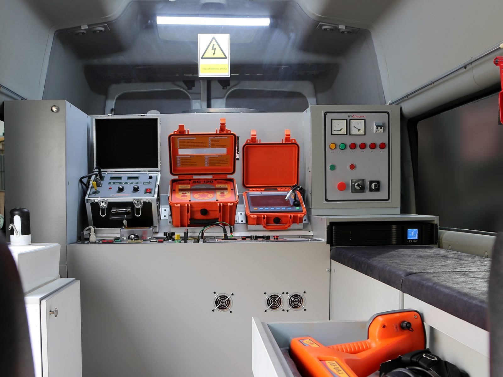 Inside the van: an instrument bench with a surge set and two orange instrument cases, a control panel with meters, a UPS, and a pull-out drawer holding a hand-held receiver and headphones.